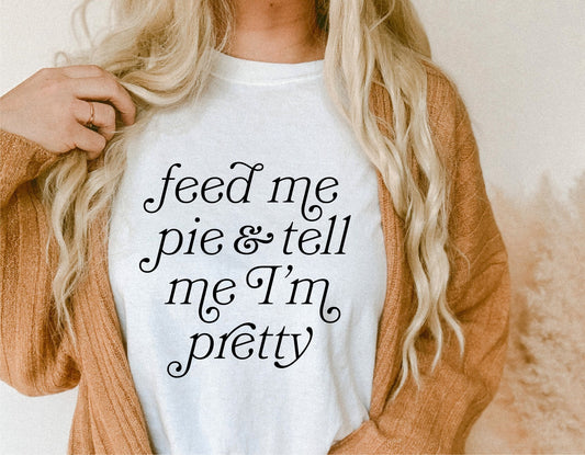 Woman wearing white t-shirt with 'Feed Me Pie and Tell Me I'm Pretty' design, autumn cardigan, funny fall SVG, Thanksgiving style.