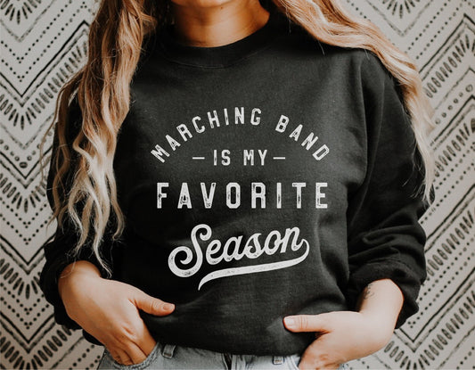 Woman wearing a black sweatshirt with 'Marching Band is my Favorite Season' text design.