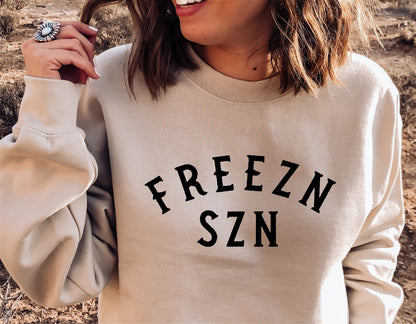 Woman wearing a beige sweatshirt with 'FREEZN SZN' printed, showcasing winter fashion and funny holiday style.