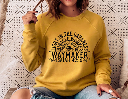 Woman in yellow sweater featuring Waymaker Isaiah 42:16 design, seated casually with patterned backdrop.