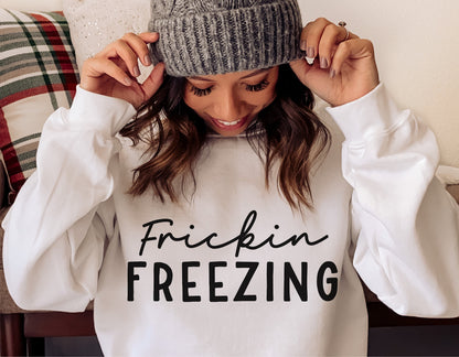 Woman wearing white sweatshirt with 'Frickin Freezing' design, winter fashion, cozy holiday wear.