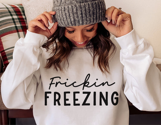 Woman wearing white sweatshirt with 'Frickin Freezing' design, winter fashion, cozy holiday wear.