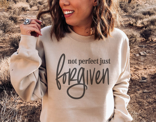 Woman wearing sweatshirt with 'Not Perfect Just Forgiven' design in desert landscape.