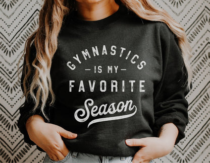Person wearing a black sweatshirt with 'Gymnastics is my Favorite Season' text design. Ideal for gymnastics enthusiasts and Cricut projects.