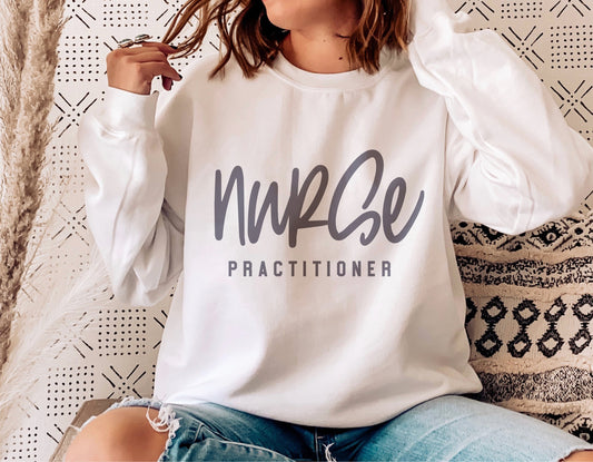 Woman wearing a white 'Nurse Practitioner' sweatshirt, sitting on a patterned cushion, perfect for nurse appreciation gifts.