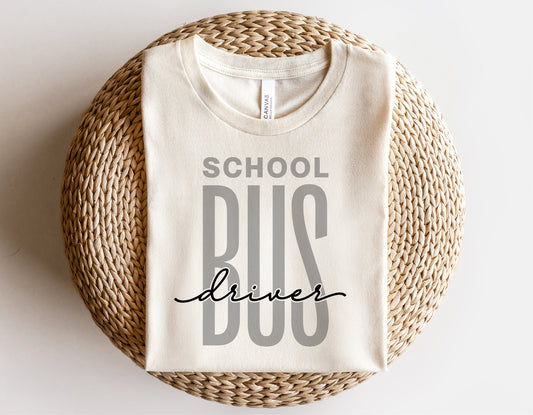 Folded white t-shirt with 'School Bus Driver' text design on woven basket, ideal for bus driver gifts and apparel.