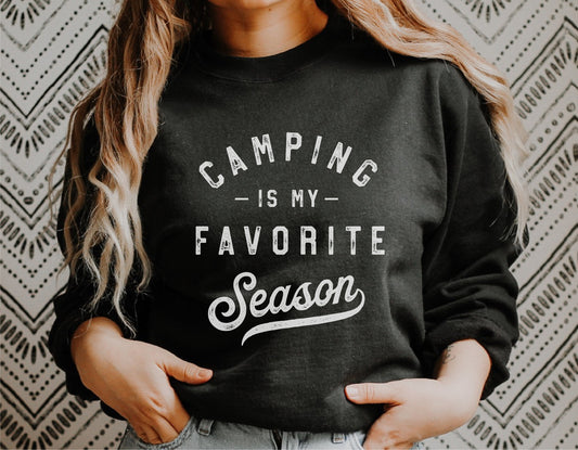 Woman wearing 'Camping Is My Favorite Season' black sweatshirt, casual outdoor style.