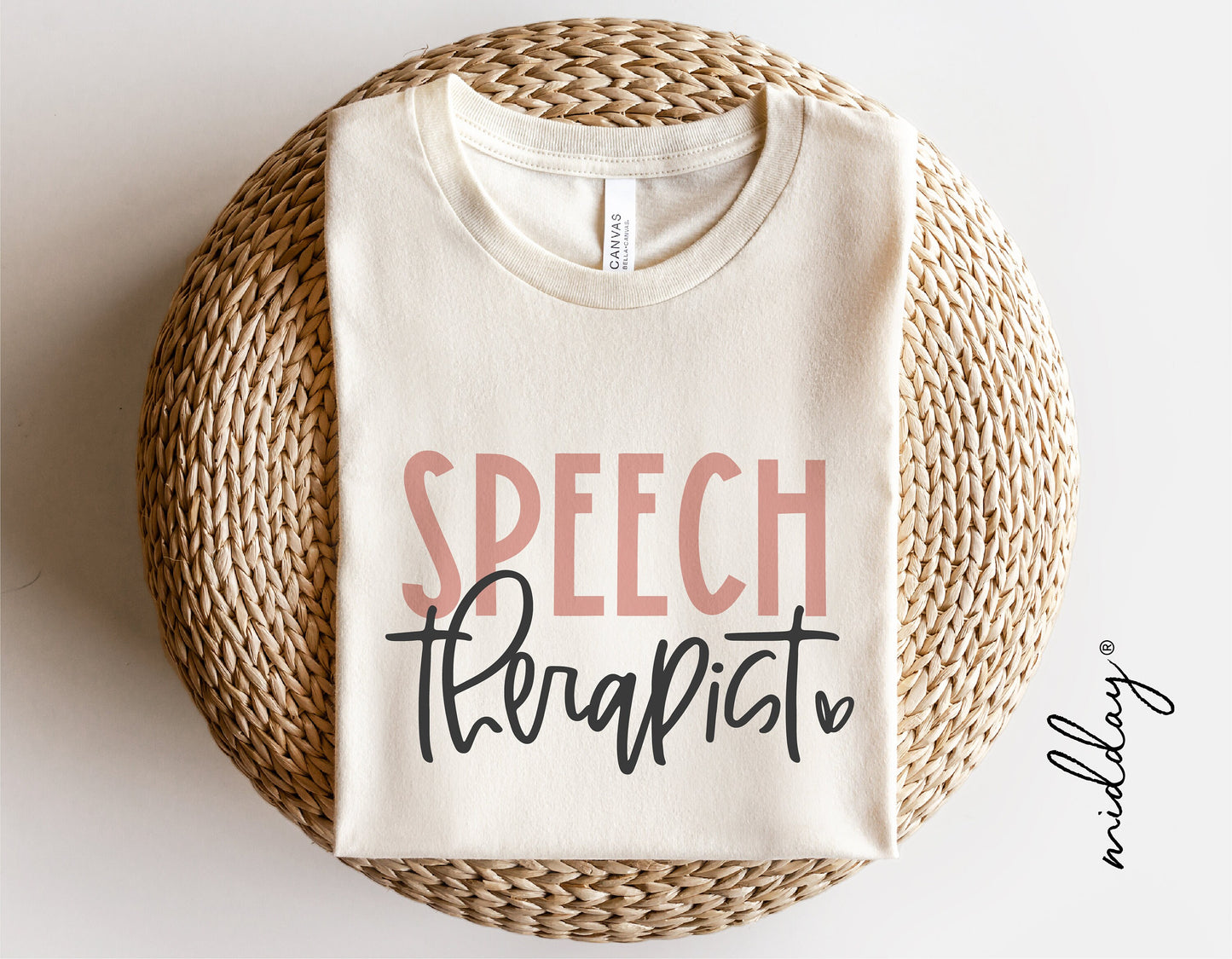 White t-shirt with 'Speech Therapist' design in pink and black fonts, styled on a woven mat.