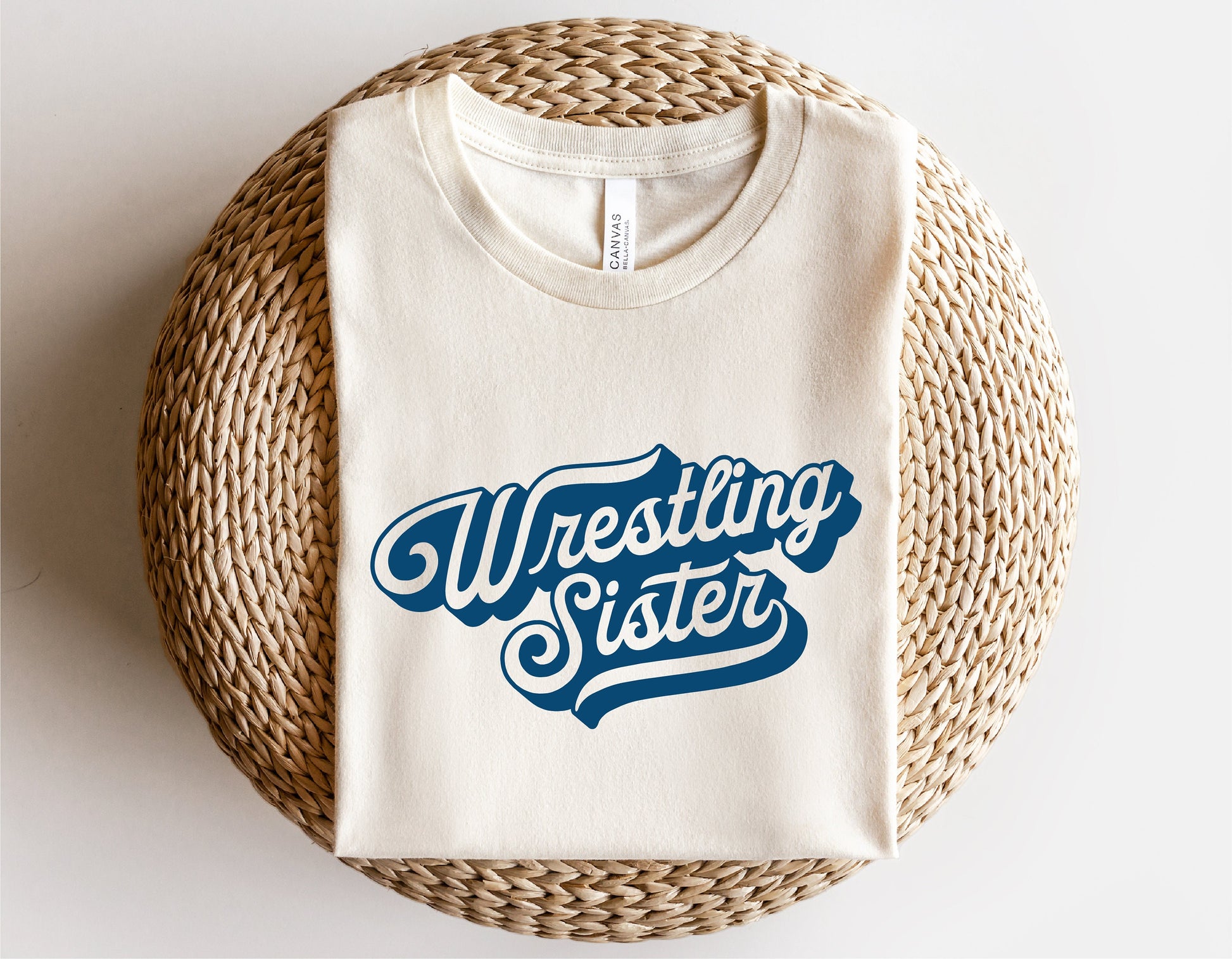 White T-shirt with 'Wrestling Sister' text design, laid on a woven basket background.