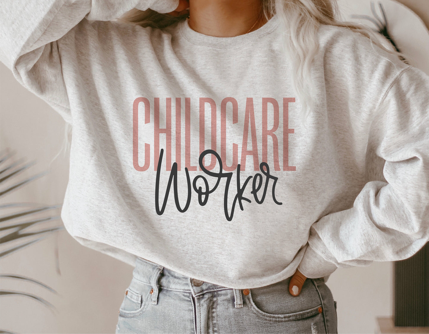 Woman wearing a gray sweatshirt with 'Childcare Worker' text in pink and black, ideal gift for daycare providers. Digital download available.