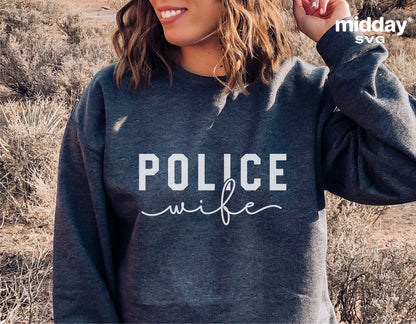Woman wearing a gray sweatshirt with 'Police Wife' text design in a natural outdoor setting.