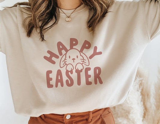 Woman wearing a beige shirt with "Happy Easter" and bunny graphic, ideal for Easter celebrations and festive crafting projects.