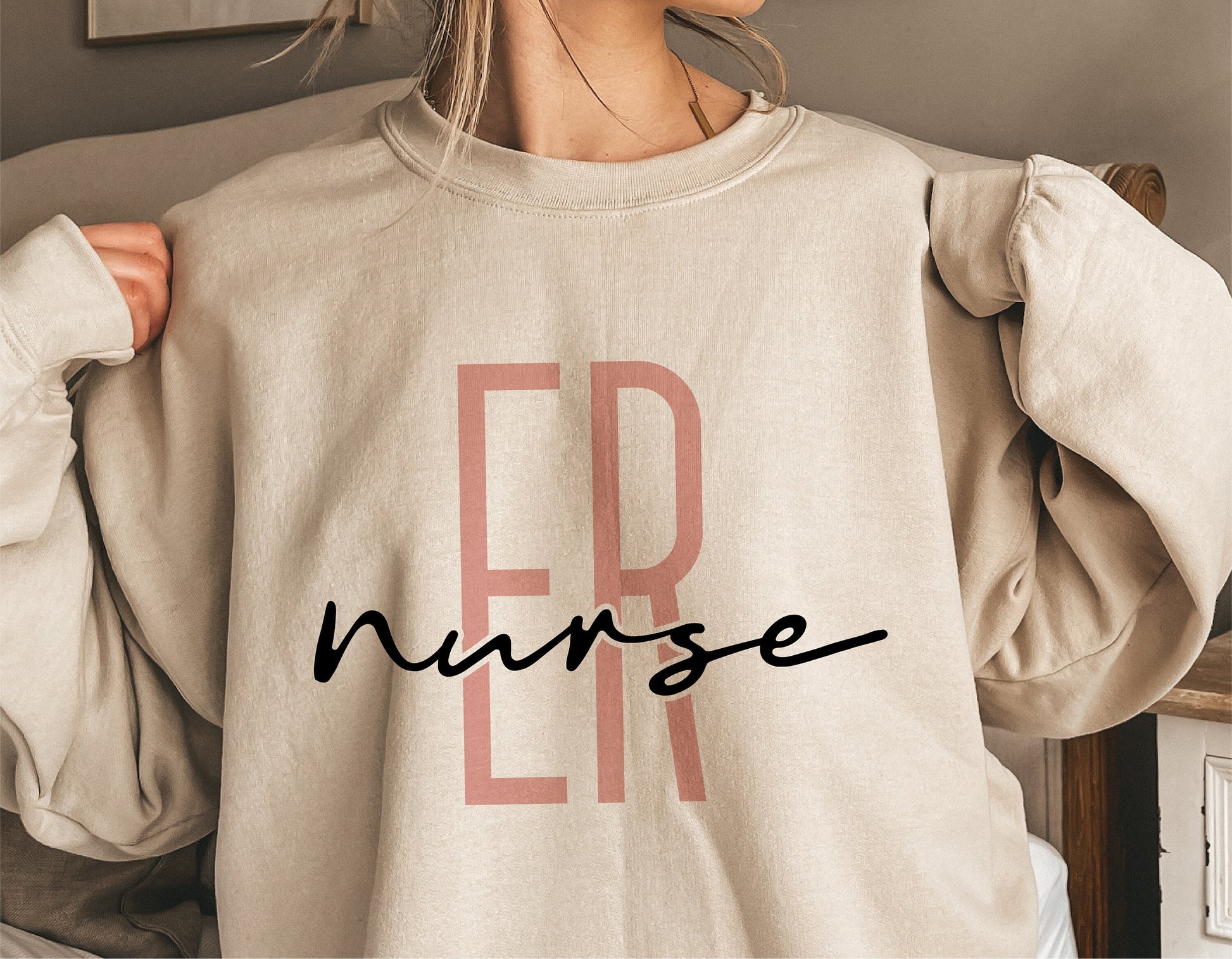 Person wearing a beige sweatshirt with 'ER Nurse' printed on the front in bold letters, showcasing nurse-themed apparel design.