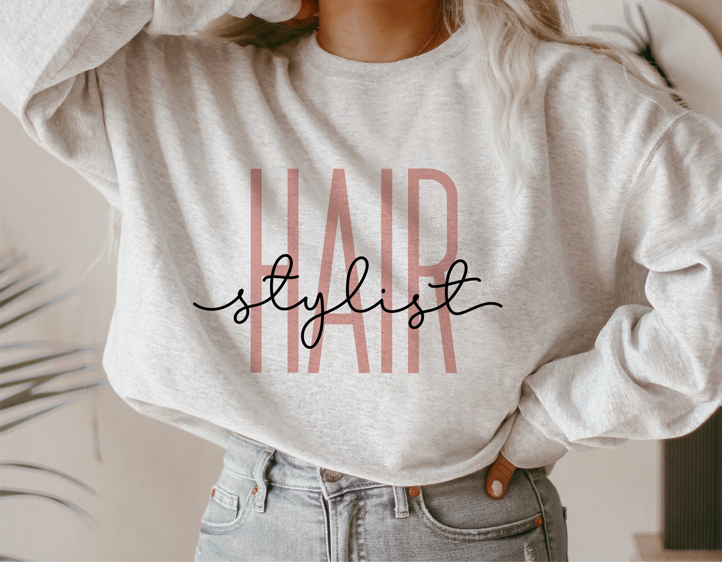 Woman wearing a gray sweatshirt featuring a 'Hair Stylist' design in pink and black font.
