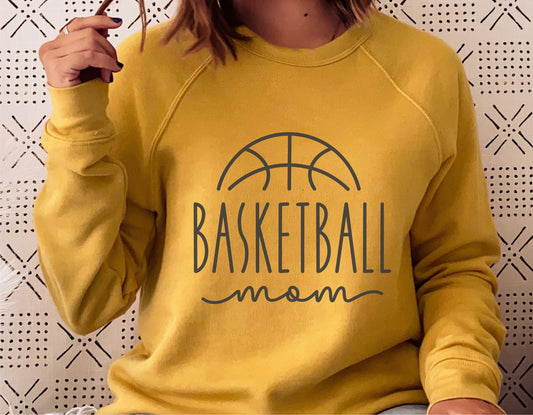 Woman wearing yellow sweatshirt with 'Basketball Mom' design, ideal for sports fan apparel options like shirts, hoodies, tumblers.