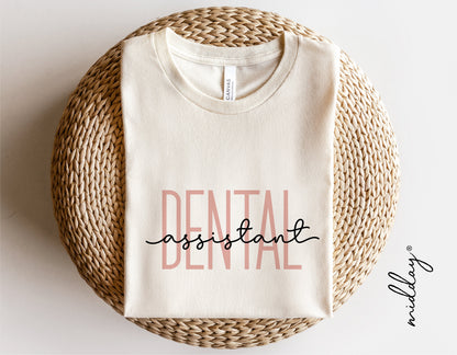 White t-shirt with 'Dental Assistant' text design, ideal for dental professionals, placed on a woven surface. Perfect for Cricut projects.
