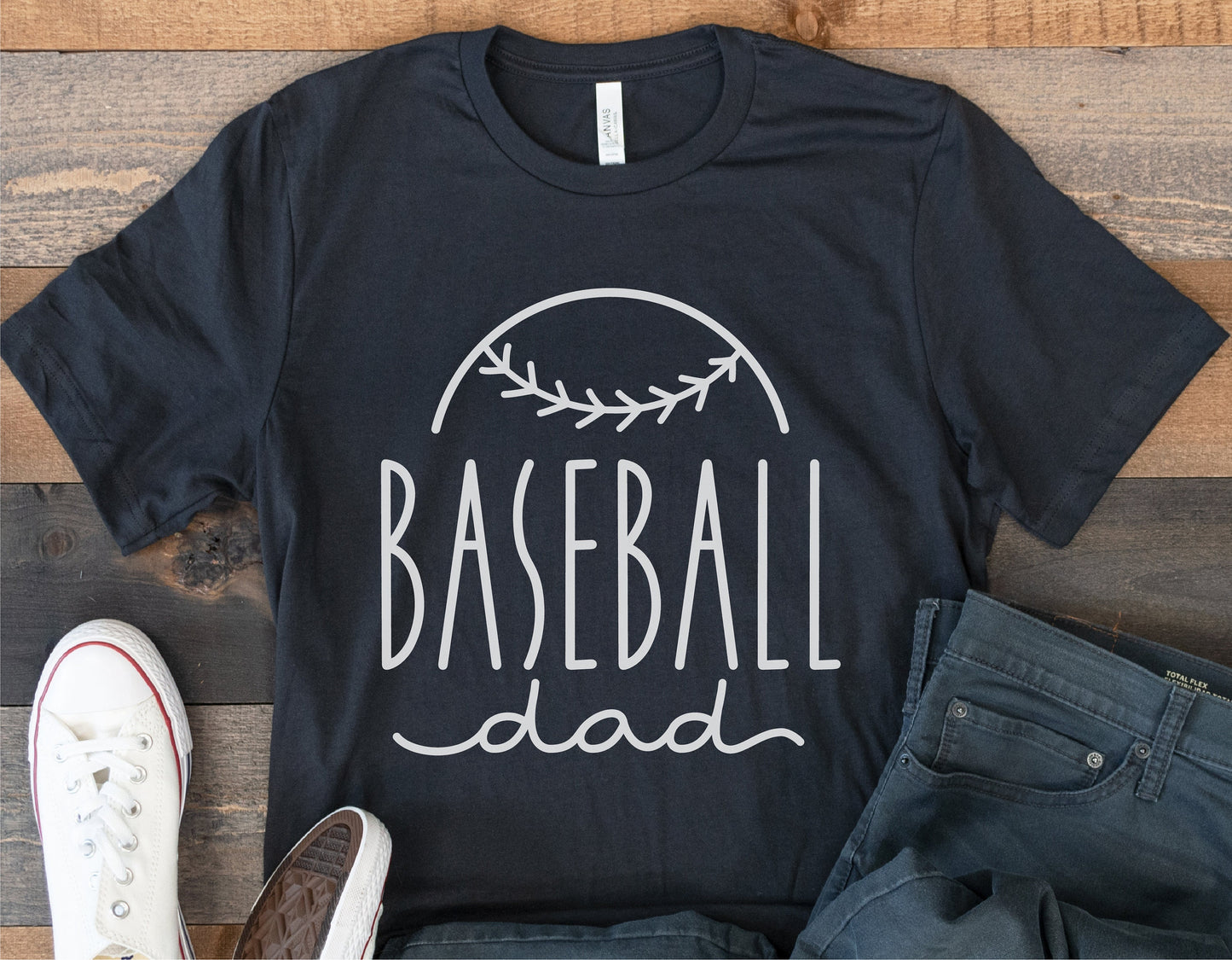 Black 'Baseball Dad' t-shirt with baseball seam graphic, styled with white sneakers and jeans, ideal for Father's Day gift.