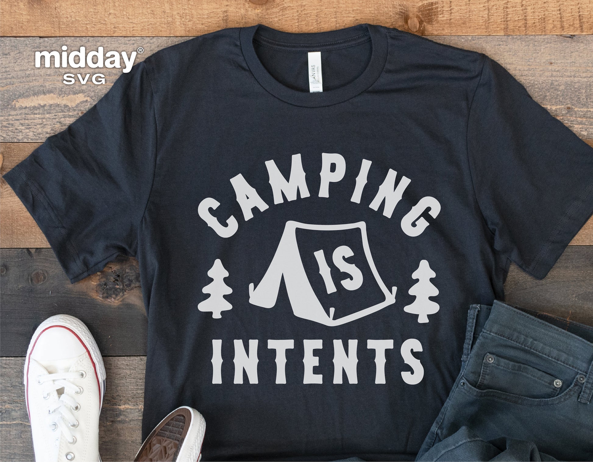 Black t-shirt with 'Camping is Intents' design, featuring a tent and trees, laid out on wooden surface with casual shoes and jeans.