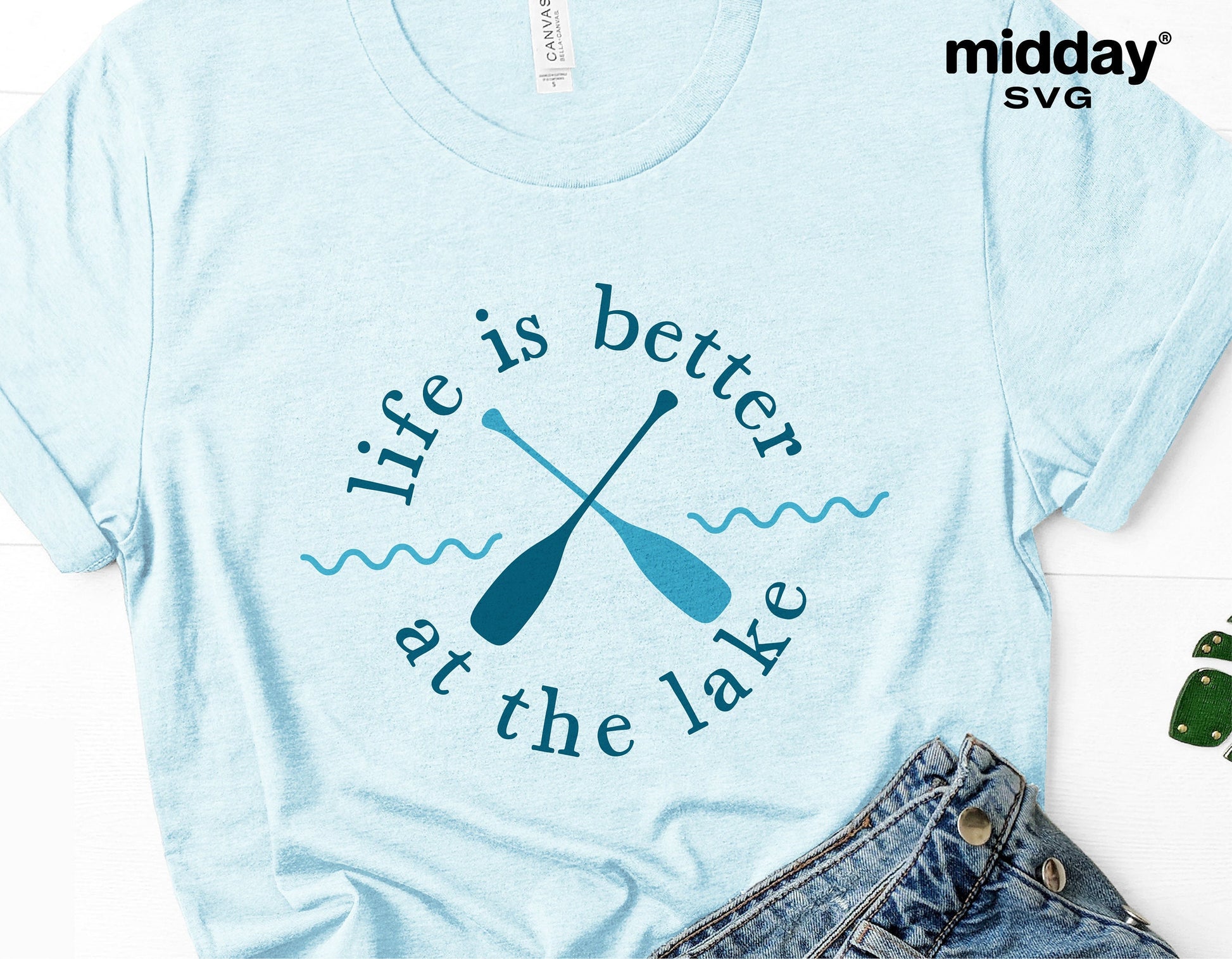 Light blue t-shirt with 'Life is better at the lake' design featuring crossed paddles, ideal for lake vacation or camping enthusiasts.