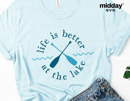 Light blue t-shirt with 'Life is better at the lake' design featuring crossed paddles, ideal for lake vacation or camping enthusiasts.