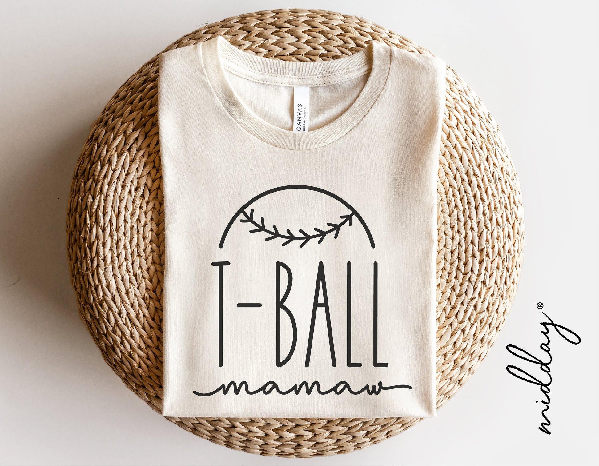 White T-ball Mamaw shirt with baseball graphic, folded on a woven round mat, ideal for Cricut and Silhouette projects.