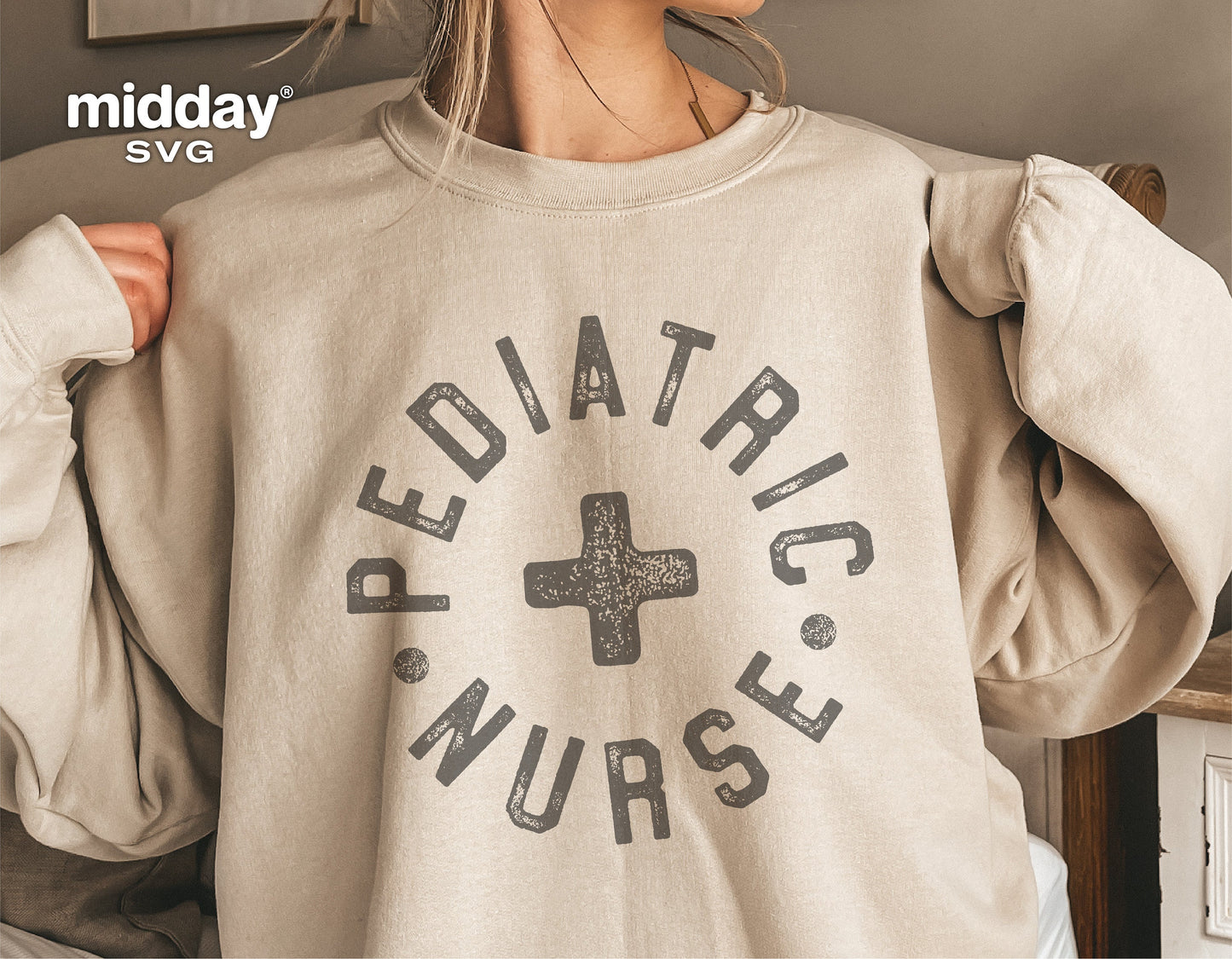 Woman wearing a beige sweatshirt with 'Pediatric Nurse' design featuring a plus symbol, ideal for medical professionals.