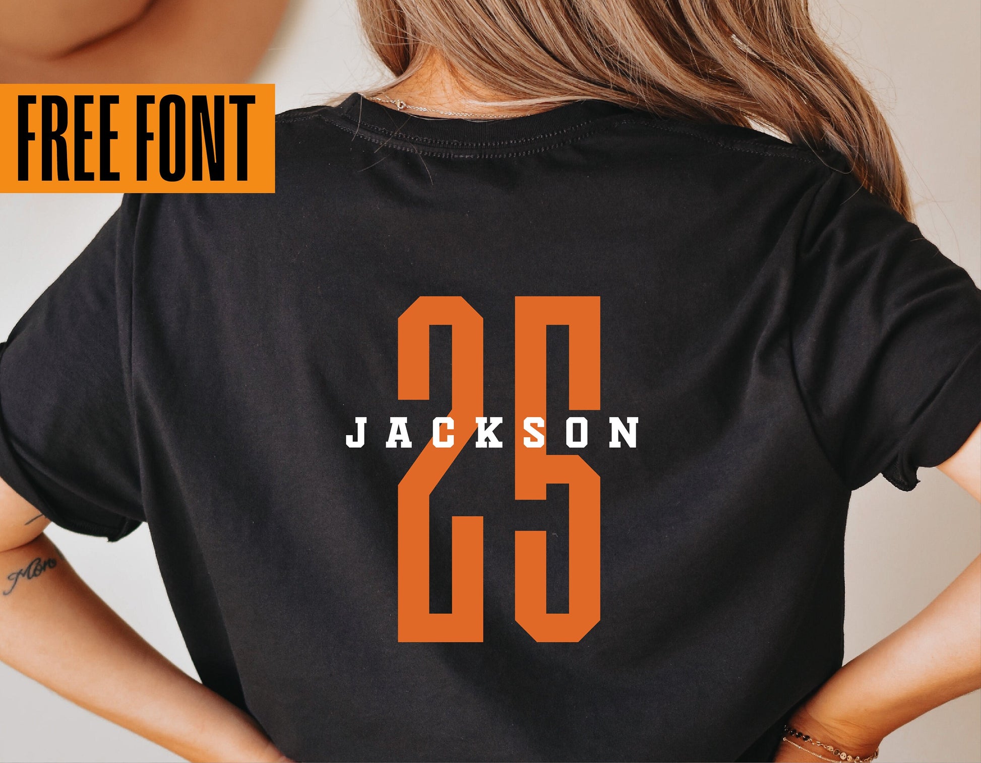 Rear view of a person wearing a black shirt with "Jackson 25" printed in bold orange and white letters, featuring a free font offer.