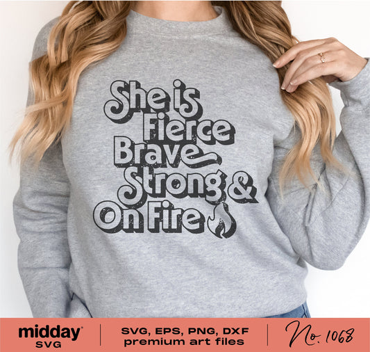 Woman wearing a gray sweatshirt with 'She is Fierce Brave Strong & On Fire' text, featuring a feminine empowerment design.